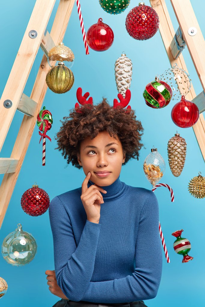 подарок родителям какой выбрать photo-serious-dark-skinned-woman-with-curly-hair-thinks-what-present-buy-husband-new-year-dressed-casual-turtleneck-reindeer-horns-surrounded-by-shiny-baubles-hanging-ladder-min.jpg